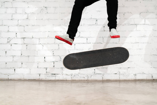 Skateboarder performing skateboard trick - kick flip on concrete. Olympic athlete practicing jump on white background, preparing for competition. Extreme sport, youth culture, urban sport - Foto, Imagen