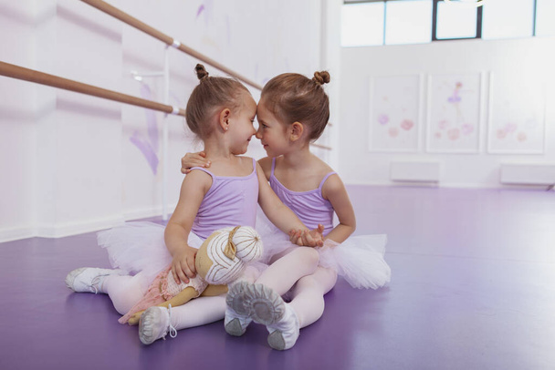 Adorable little ballerinas rubbinh noses, having fun at ballet school, copy space. Cute little sisters touching nose to nose, cuddling at dance studio - Photo, Image