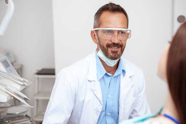 Allegro dentista maschio maturo sorridente mentre parla con la sua paziente dopo il controllo dentale
 - Foto, immagini