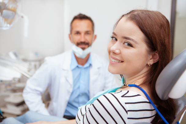 Обаятельная счастливая женщина улыбается камере, сидя в стоматологическом кресле после обследования зубов
 - Фото, изображение