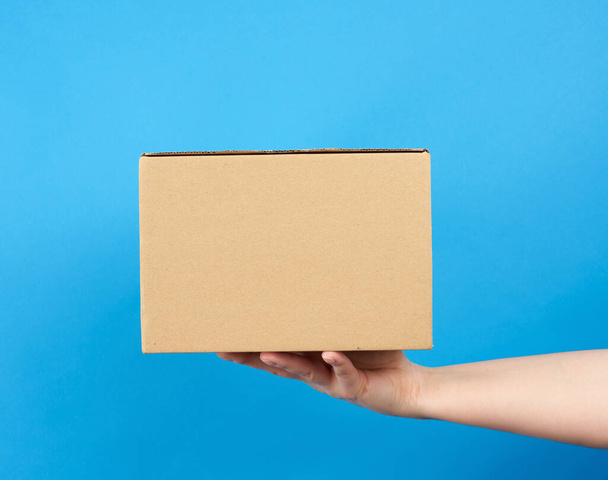 hand holds a brown cardboard box of paper on a blue background, close up - Photo, Image