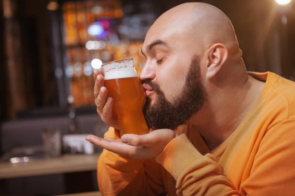Közelkép egy szakállas férfiról, aki egy pohár finom sört csókol a kocsmában. - Fotó, kép