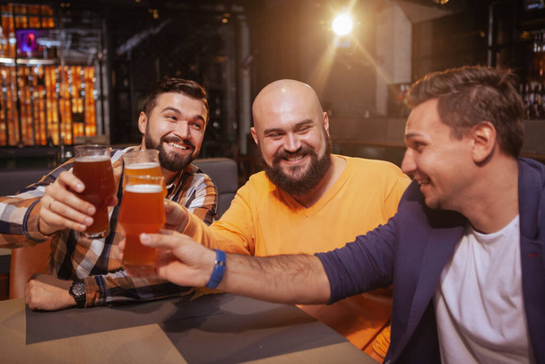 Trzech przyjaciół śmieje się w pubie, pijąc razem kieliszki. - Zdjęcie, obraz