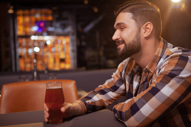 Foto profilo di un bell'uomo barbuto sorridente gioiosamente, bere deliziosa birra artigianale al pub, spazio copia
 - Foto, immagini