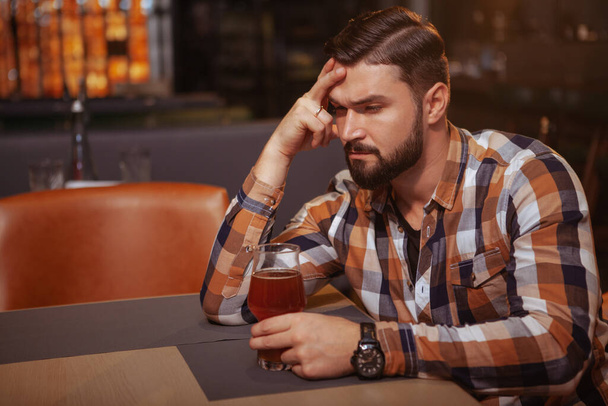 Депресивний молодий чоловік п'є сам у барі. Красивий чоловік виглядає п'яним, сидячи один біля бару зі склянкою пива
 - Фото, зображення