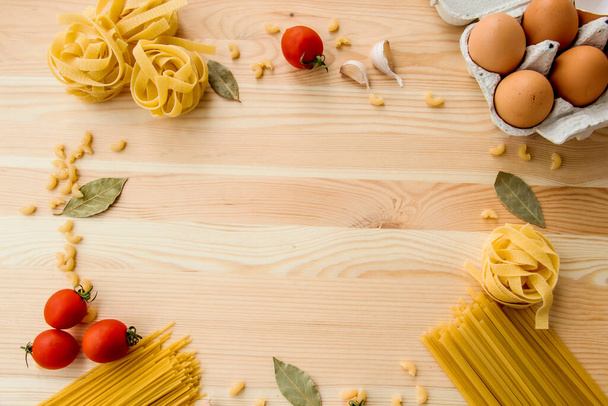 Cooking food background with free space for text. Composition with pasta, tomato, eggs, garlic, bay leaf over the wood background. Ingredients for cooking with copy space. Top view with copy space - Fotografie, Obrázek