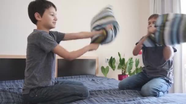 幸せな子供たちは寝室のベッドで枕の戦いをしている。子供たちは面白いゲームを楽しんでいます。ホームエンターテイメントに滞在する - 映像、動画