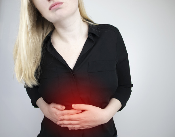 Μια γυναίκα κρατάει το στομάχι του. Πόνος στην κοιλιακή κοιλότητα. Η έννοια των ασθενειών του στομάχου και του πεπτικού συστήματος - Φωτογραφία, εικόνα