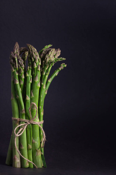 A tied bunch of asparagus standing vertical on black background - Foto, imagen