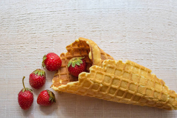 O conceito de deliciosa casa de assar e verão. Um cone de waffle com morangos derramado sobre um fundo de madeira branco feito de tábuas no estilo de um loft com um espaço de cópia
. - Foto, Imagem