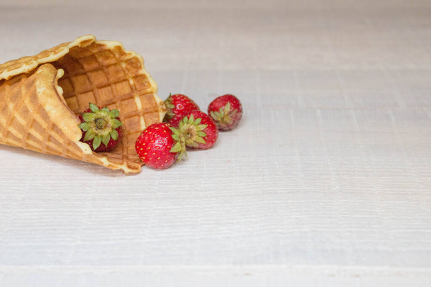O conceito de deliciosa casa de assar e verão. Um cone de waffle com morangos derramado sobre um fundo de madeira branco feito de tábuas no estilo de um loft com um espaço de cópia
. - Foto, Imagem