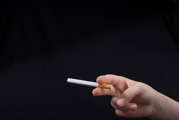 Main tient une cigarette sur fond noir - Photo, image