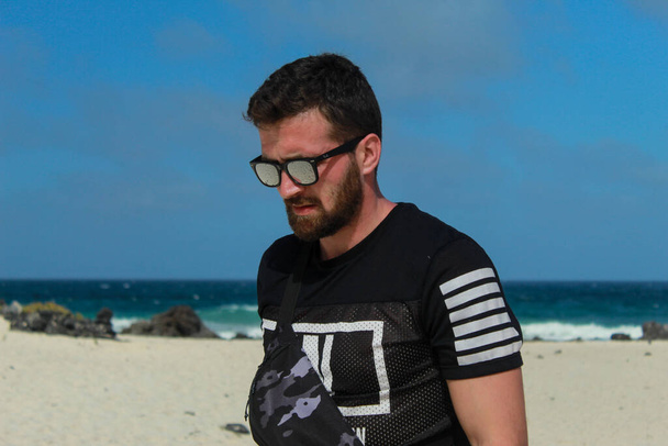 modelo caminando en la playa con una camiseta, riñonera y gafas negras
 - Foto, imagen