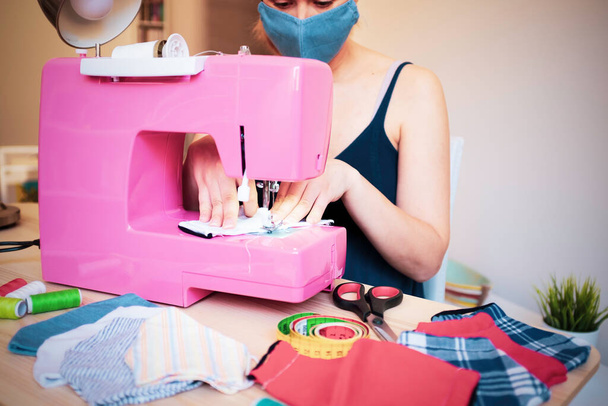 Mujer que trabaja con la máquina de coser haciendo mascarilla médica de moda para prevenir y detener la propagación del coronavirus - Concepto de fabricación casera - Reutilización de ropa usada - Enfoque principal en las manos
 - Foto, imagen