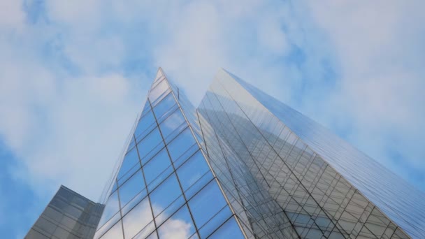 mirando un detalle del extremo puntiagudo de un rascacielos cubierto de vidrios espejados que destaca en el cielo azul donde se mueven nubes blancas que se reflejan en la fachada del edificio
 - Imágenes, Vídeo