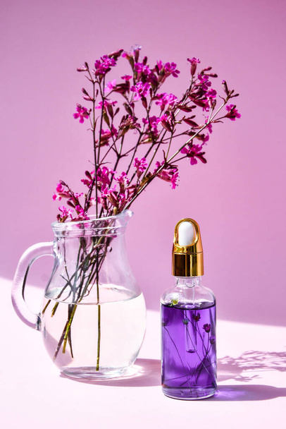 Spa Tropfflasche mit Essenz trockene Blumen und kleine rosa Blumen auf rosa Hintergrund, Nahaufnahme, Kopierraum, Hautpflegeprodukte, Naturkosmetik für zu Hause Wellness-Behandlung - Foto, Bild