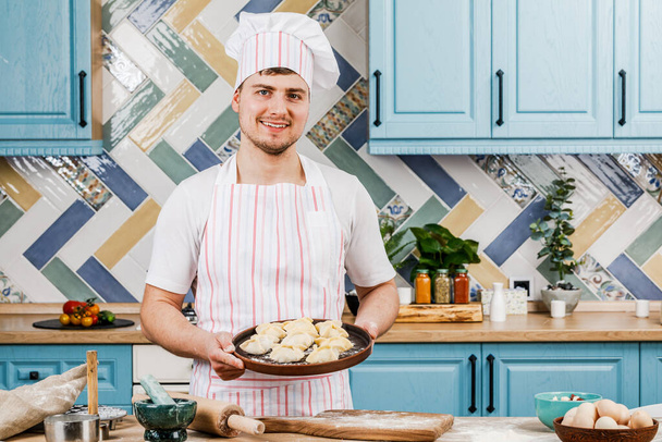 Kucharz w kuchni trzyma pierogi w rękach i wskazuje na nie ręką. Koncepcja gotowania - Zdjęcie, obraz
