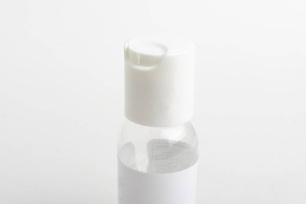 Ένα κοντινό πλάνο προϊόντος του πάνω λευκού πώματος μιας διάφανης φιάλης αποστειρωτήρα χεριών μεγέθους τσέπης που τοποθετείται σε ένα απλό λευκό φόντο. - Φωτογραφία, εικόνα