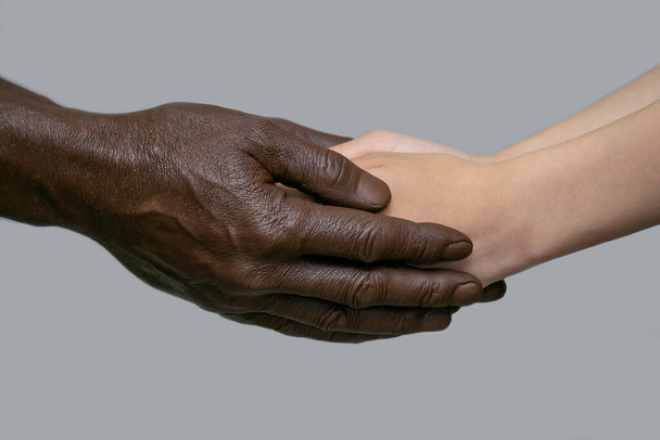 Black male hands hold white female human hands in their palms. The concept of inter-racial friendship, love, respect, and the fight against racism. Copy of the space, gray isolated background. - 写真・画像