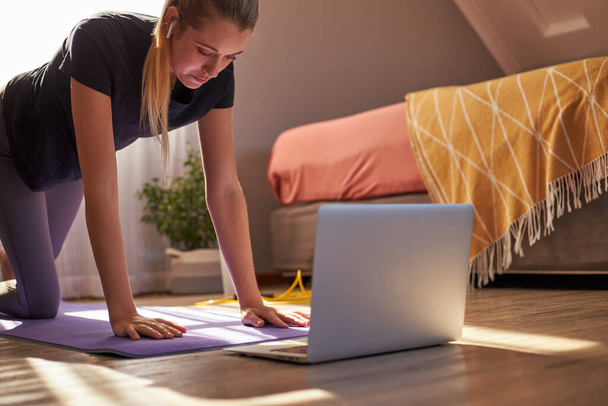 Молодая женщина, участвующая в онлайн-фитнес-классе перед ноутбуком. - Фото, изображение