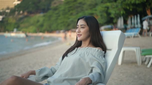 Holiday concept. An Asian woman is resting on a bench by the beach. 4k Resolution. - Záběry, video