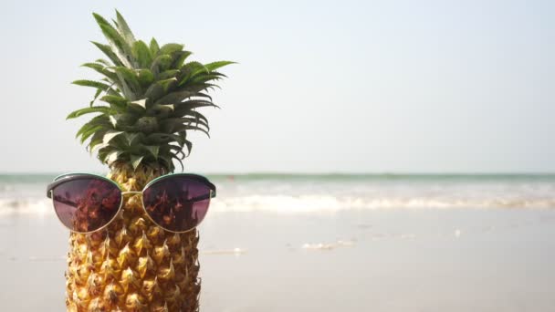 Ananász gyümölcs napszemüvegben a tengerparton. Trópusi nyaralás koncepciója - Felvétel, videó