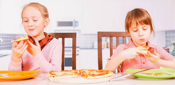 En iyi yiyeceklerin sembolü olarak ellerinde pizza dilimleri tutan iki sevimli küçük kız çocuğu portresi. Yatay resim. - Fotoğraf, Görsel
