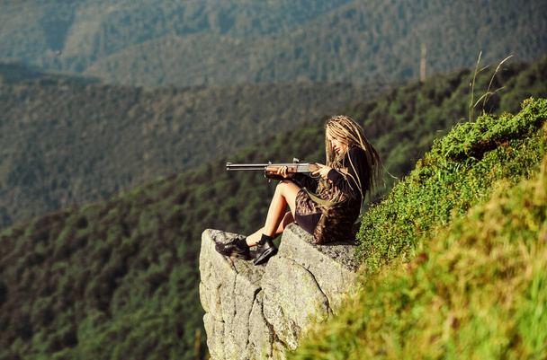Hunter mountains landscape background. Sexy warrior. Woman attractive long hair pretty face hold rifle for hunting. Amazon girl sit on cliff prepare gun for hunting. Aiming concept. Hunting season - Fotografie, Obrázek
