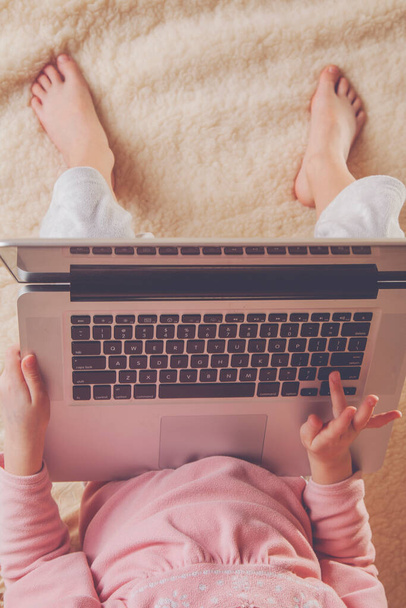 Pequeña niña linda que se divierte utilizando el ordenador portátil en su dormitorio
 - Foto, imagen