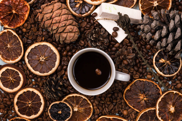 A white Cup of coffee on coffee beans, on a light blue wooden table. Wooden table. Fir cones on the table. white marshmallow. Dried citrus. Brown background. - Fotó, kép
