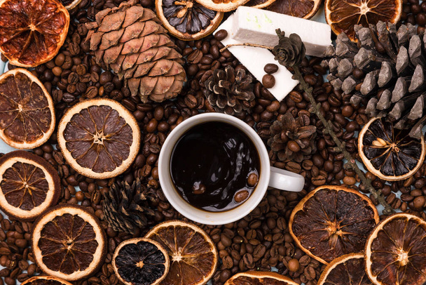 A white Cup of coffee on coffee beans, on a light blue wooden table. Wooden table. Fir cones on the table. white marshmallow. Dried citrus. Brown background. - Photo, Image