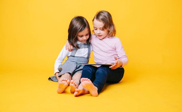 Two girls use a digital tablet on a yellow background - Foto, afbeelding