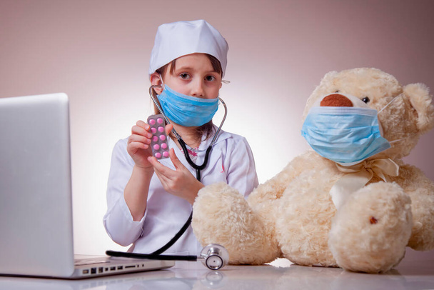Kis aranyos gyermek lány orvos védő arc maszk adja a tablettákat a beteg Teddy maci. Vírus, egészségügy és orvostudomány. Vízszintes kép. - Fotó, kép
