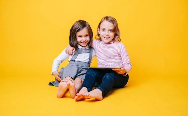 Two girls use a digital tablet on a yellow background - Photo, Image