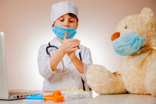 Kis aranyos lány játszik orvos védő arc maszk és megmutatja Teddy maci, hogyan kell mosni a kezét profilaktikus a koronavírus. A gyermek kezére való szelektív összpontosítás. - Fotó, kép