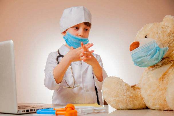 保護顔のマスクの小さなかわいい子供の女の子の医者はテディベアコロナウイルスの予防のための手を洗う方法を示しています。子供の手と指に焦点を当てます. - 写真・画像