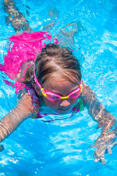 Szczęśliwego dzieciństwa. Młoda dziewczynka pływanie w basenie i zabawy rekreacyjne. Obraz pionowy. - Zdjęcie, obraz