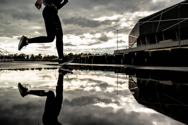 スポーツの背景。運動中の女性ランナーの強い運動脚。雨の後、屋外で心臓のトレーニングを行う女性. - 写真・画像