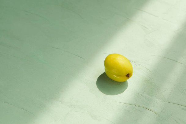 Albaricoque amarillo-verde inmaduro en el sol de la mañana sobre un fondo verde texturizado. Concepto - Comer frutas inmaduras
. - Foto, imagen