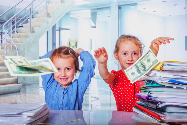 Portrét malých roztomilých holčiček pracujících v kanceláři a užívajících si sprchu z amerických bankovek. Létající peníze jako symbol zisku, bohatství, svobody a úspěchu. - Fotografie, Obrázek