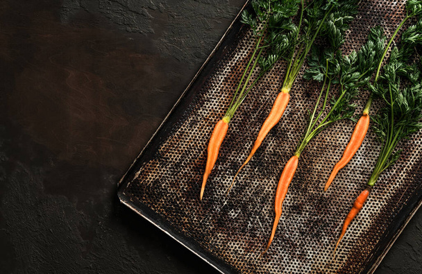 Fresh carrots for roasting on baking tray on dark background. Fresh vegetables, healthy organic food, harvest, agriculture, top view - Foto, Bild