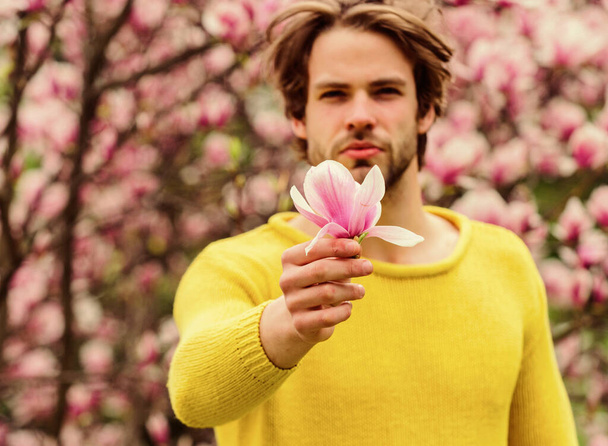 Floral cosmetics concept. Hipster enjoy blossom aroma. Unshaven man magnolia bloom. Man flowers background defocused. Hairdo styling. Spring beauty. Botany nature. Male beauty. Hair care and beauty - Photo, Image