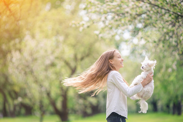 Küçük gülümseyen kız parkta oynaşıyor ve yavru köpeğe sarılıyor. - Fotoğraf, Görsel
