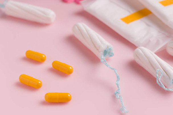 The concept of treating pain during the menstrual cycle in women. Pills and tampons on a pink background - Foto, afbeelding