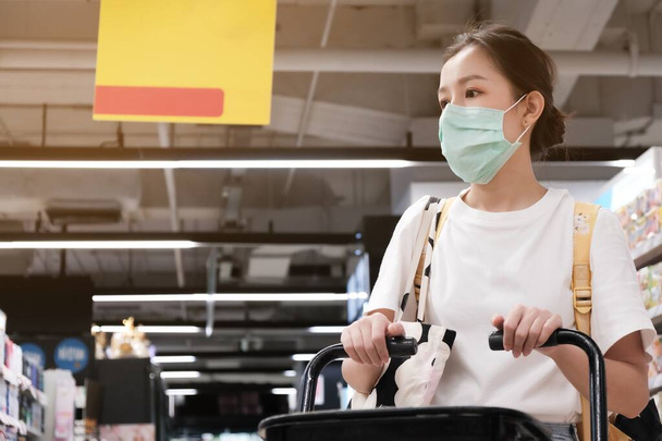 Sarı çantalı Asyalı kız süpermarkette Covid-19 'u korumak için cerrahi maske takıyor. - Fotoğraf, Görsel