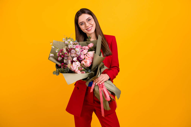 Foto van stijlvolle aantrekkelijke zakelijke dame werknemer houden grote bloemen bos collega 's verjaardag cadeau te dragen specs rood luxe kantoor blazer blauw blouse pak geïsoleerde gele kleur achtergrond - Foto, afbeelding