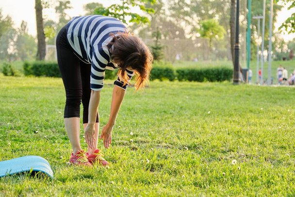 Mature woman doing fitness exercises on mat in park - Foto, Imagen
