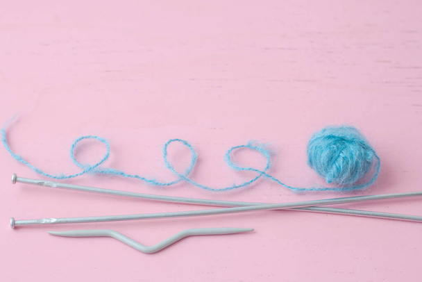 A small blue skein of mohair wool lies on the pink surface next to the knitting needles the thread is looped - Foto, Imagen