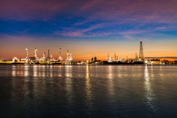 Oil refinery industry reflection on water at early morning under colorful sky of sunrise - Фото, изображение