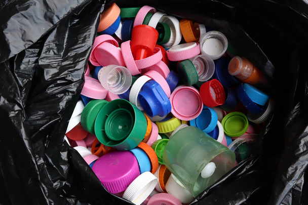 grupo de tampas de garrafa multicoloridas em saco de plástico preto, pronto para reciclagem vista superior
  - Foto, Imagem